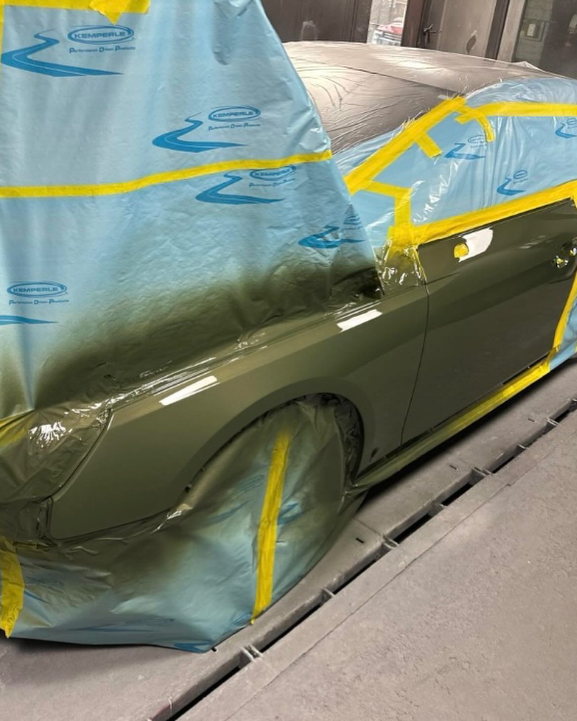 Hand using a yellow tool to remove a dent from a silver car door near the fuel door. A cloth rests nearby.