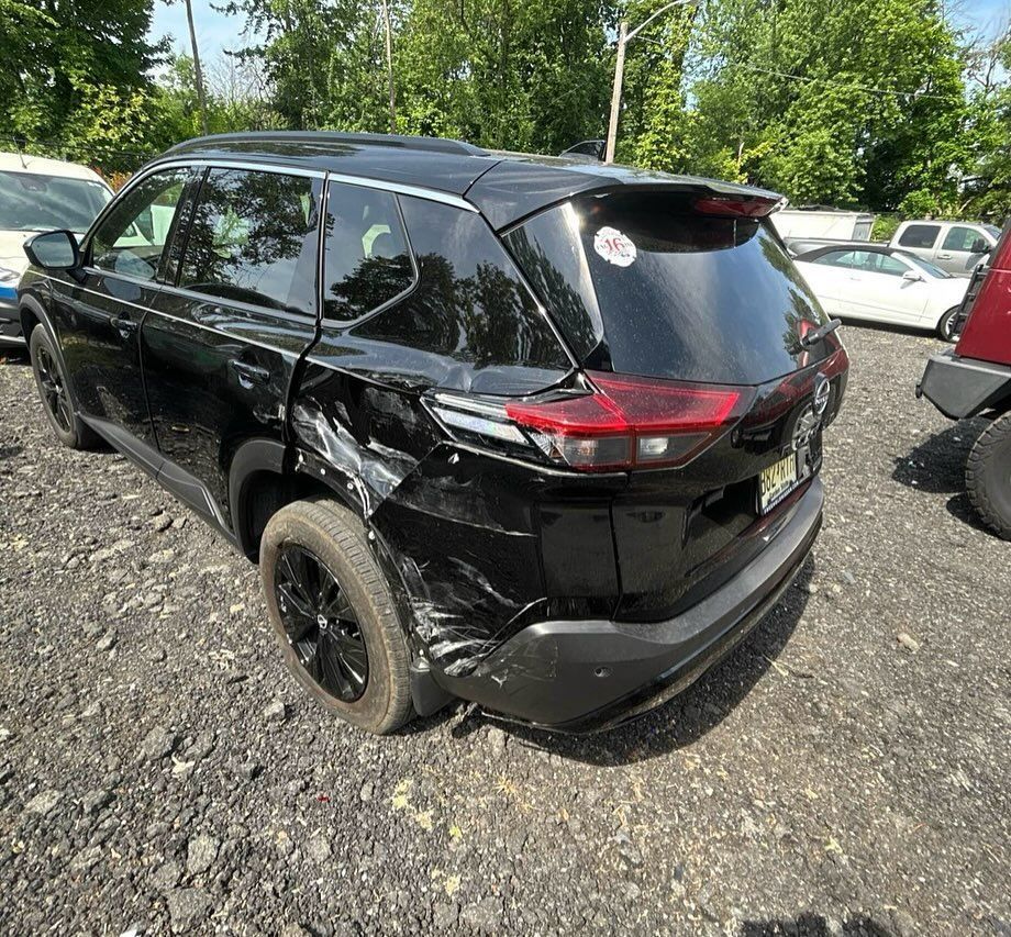 Black SUV with significant damage to the rear passenger side, parked on gravel.