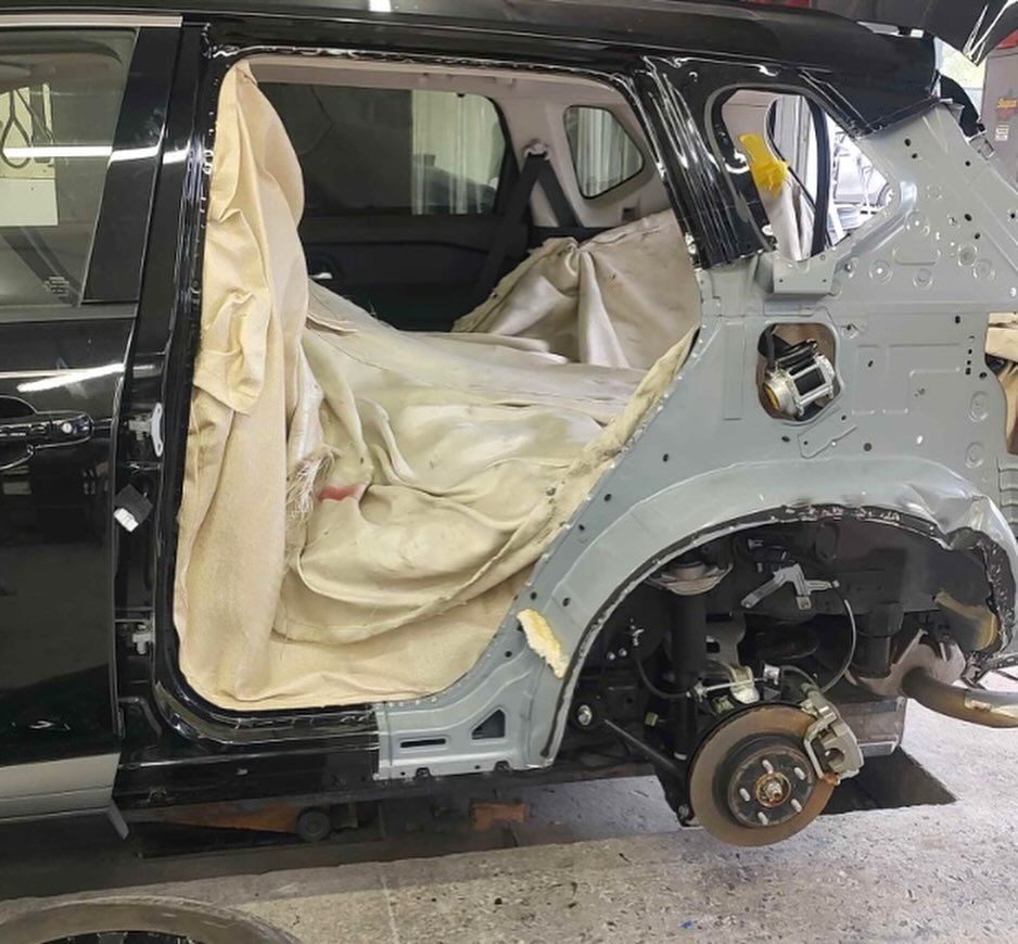 Close-up of car headlight in a repair shop; mechanic working on another car in the background.