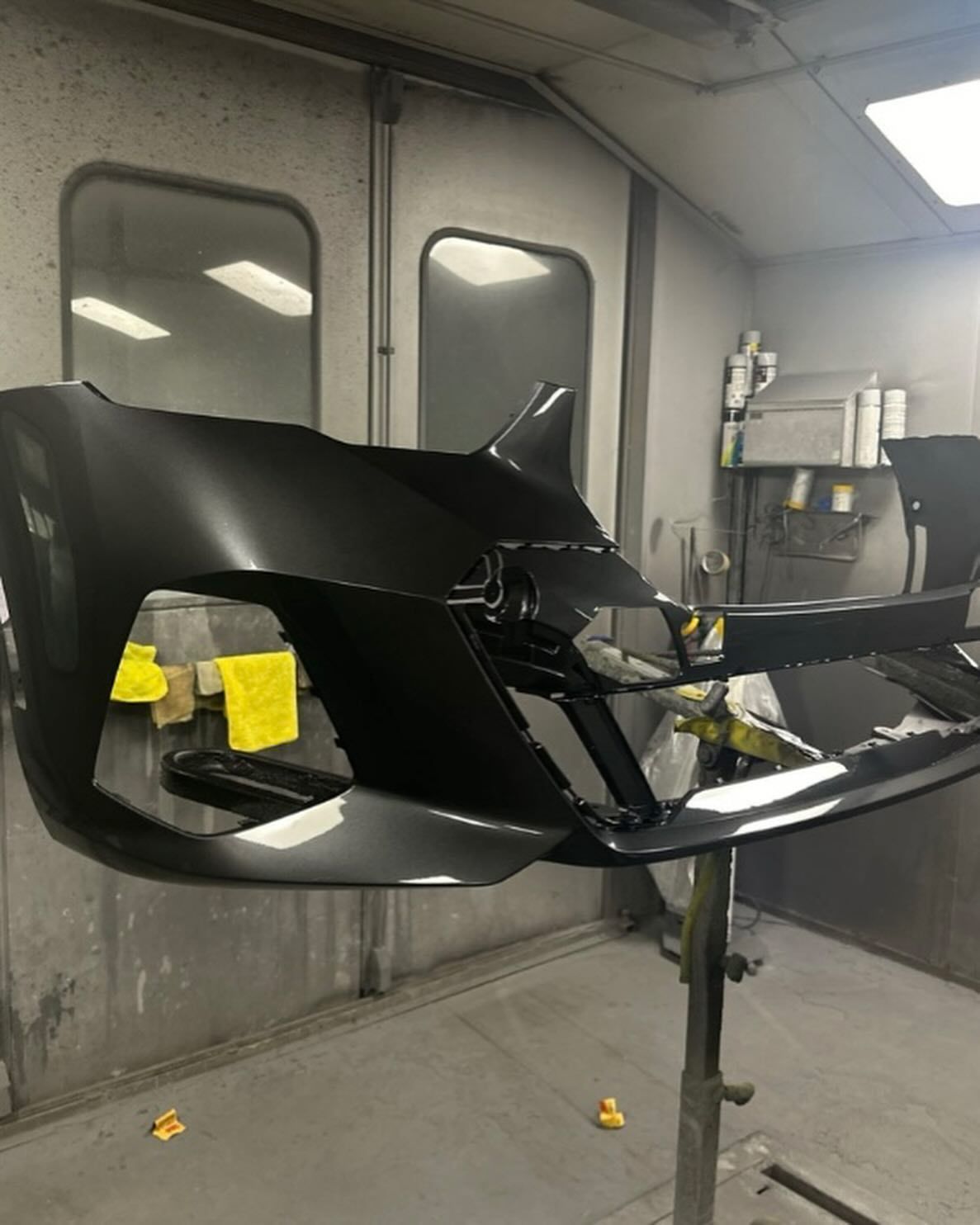 A car's blue body part being painted in a workshop. A person in white protective gear sprays it.