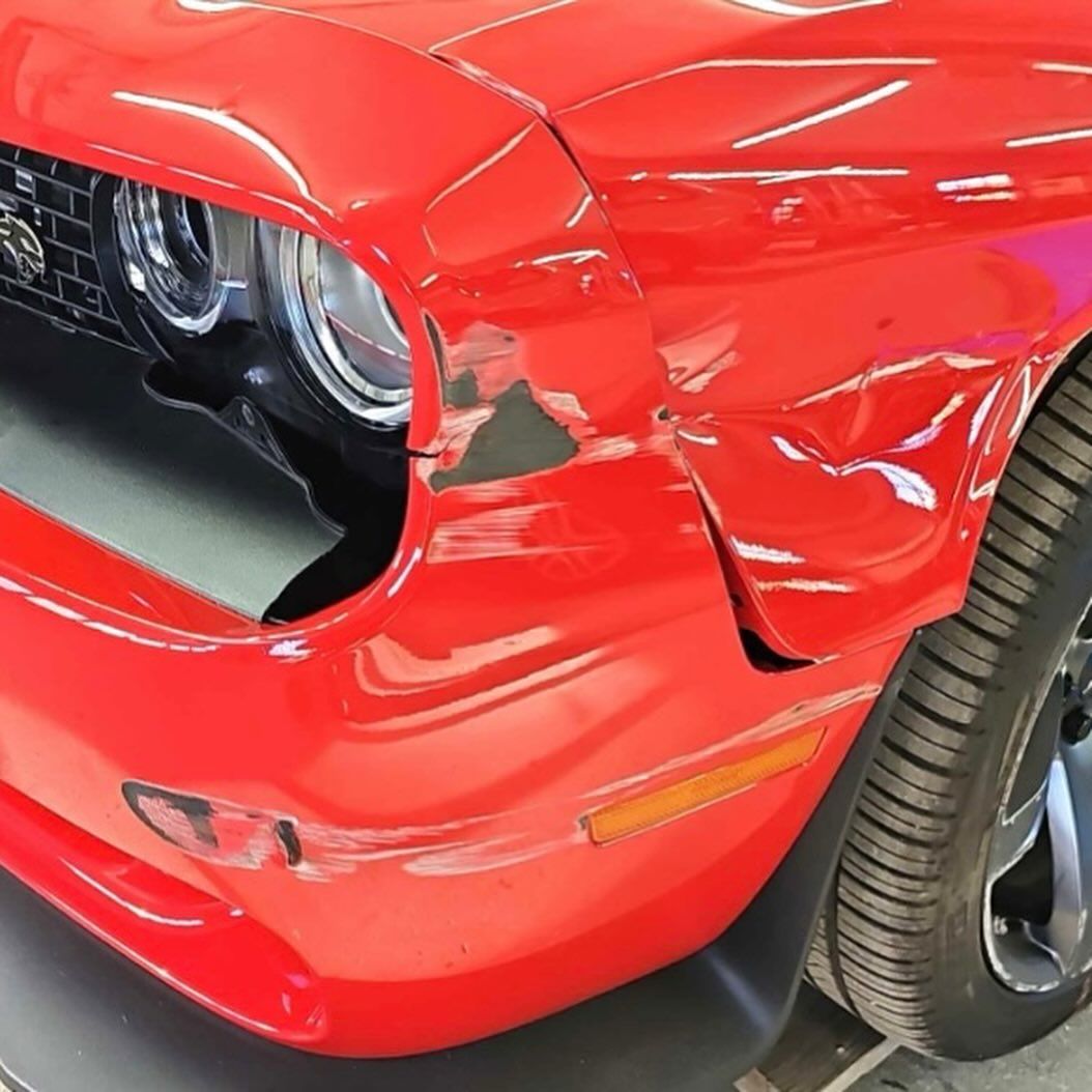 Red Dodge Challenger with damage to the front fender and headlight area.