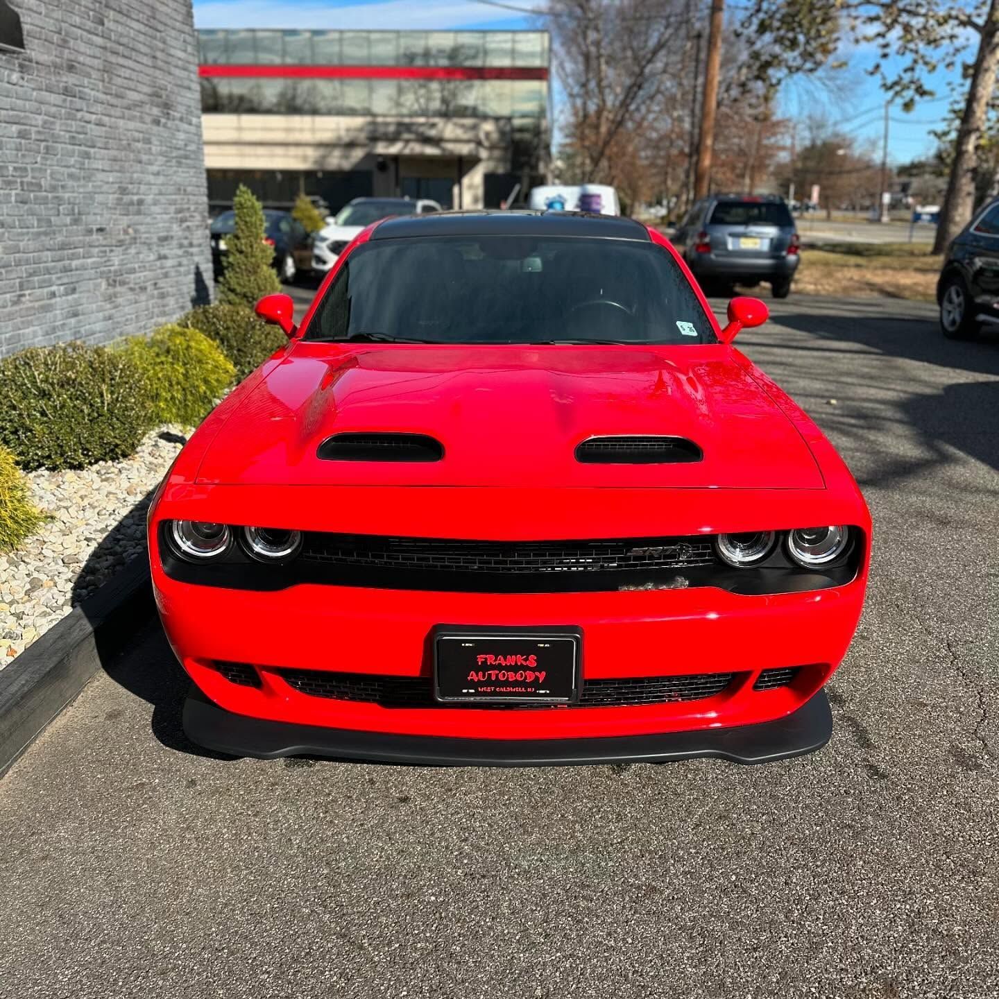 Red Dodge Challenger with black hood, parked outdoors.