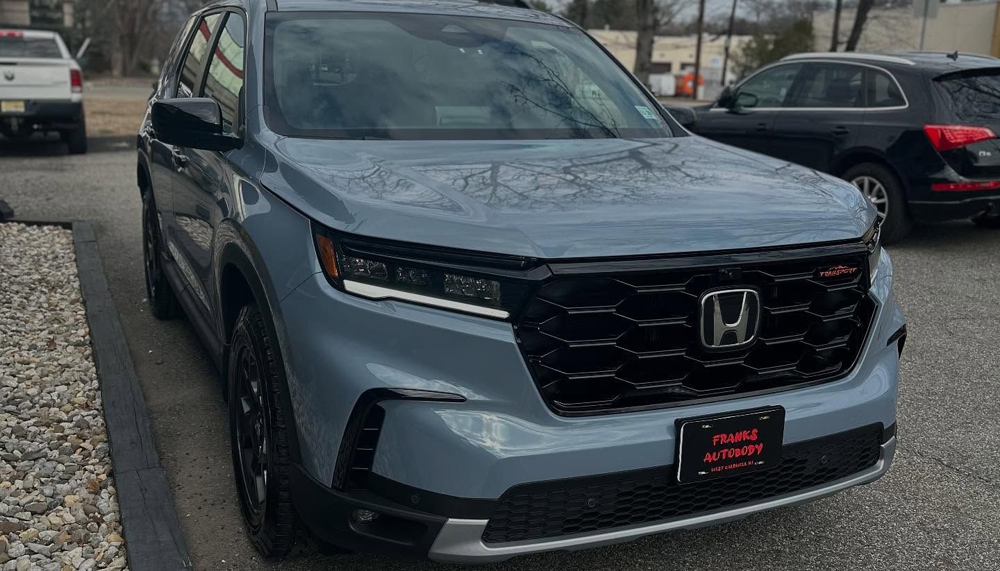 Blue Honda Pilot SUV parked in front of a building with a black grill and tires.