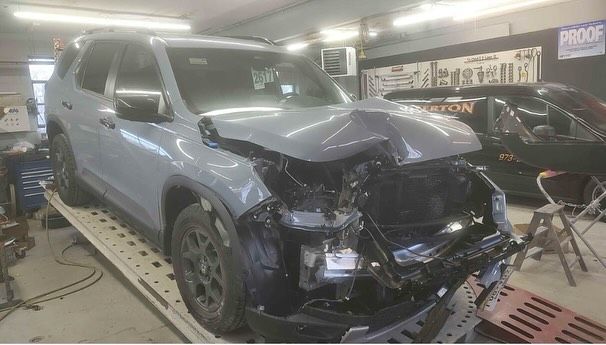 Damaged gray SUV in a repair shop, front end heavily crumpled.