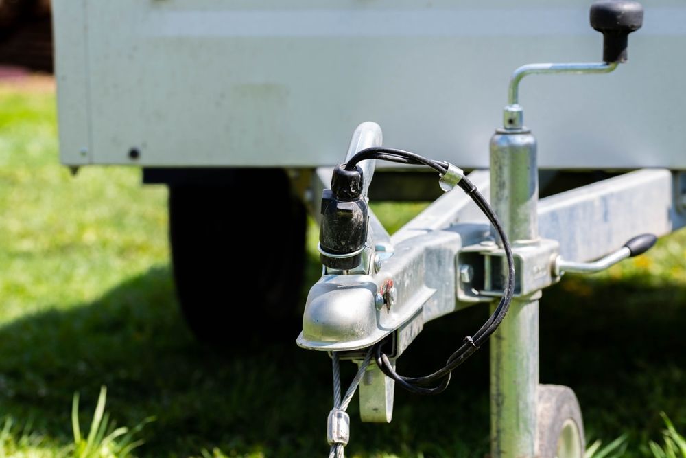 Silver trailer hitch, electrical connection, and jack with a black handle on green grass. — Caravan and Trailer Clinic Geelong in Breakwater, VIC