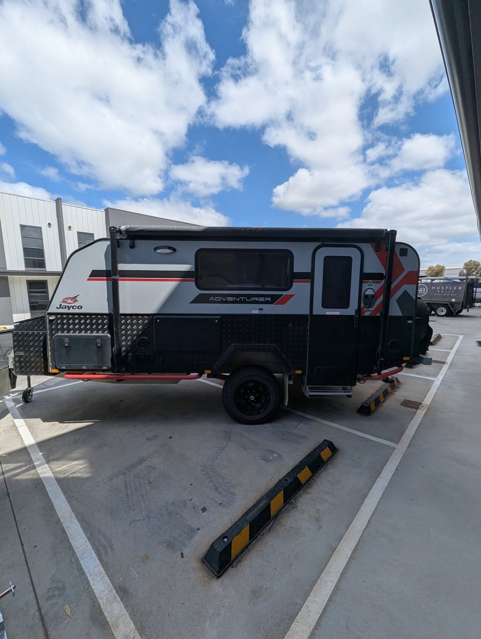 Gray, black, and red caravan parked on asphalt under a cloudy blue sky. — Caravan and Trailer Clinic Geelong in Breakwater, VIC