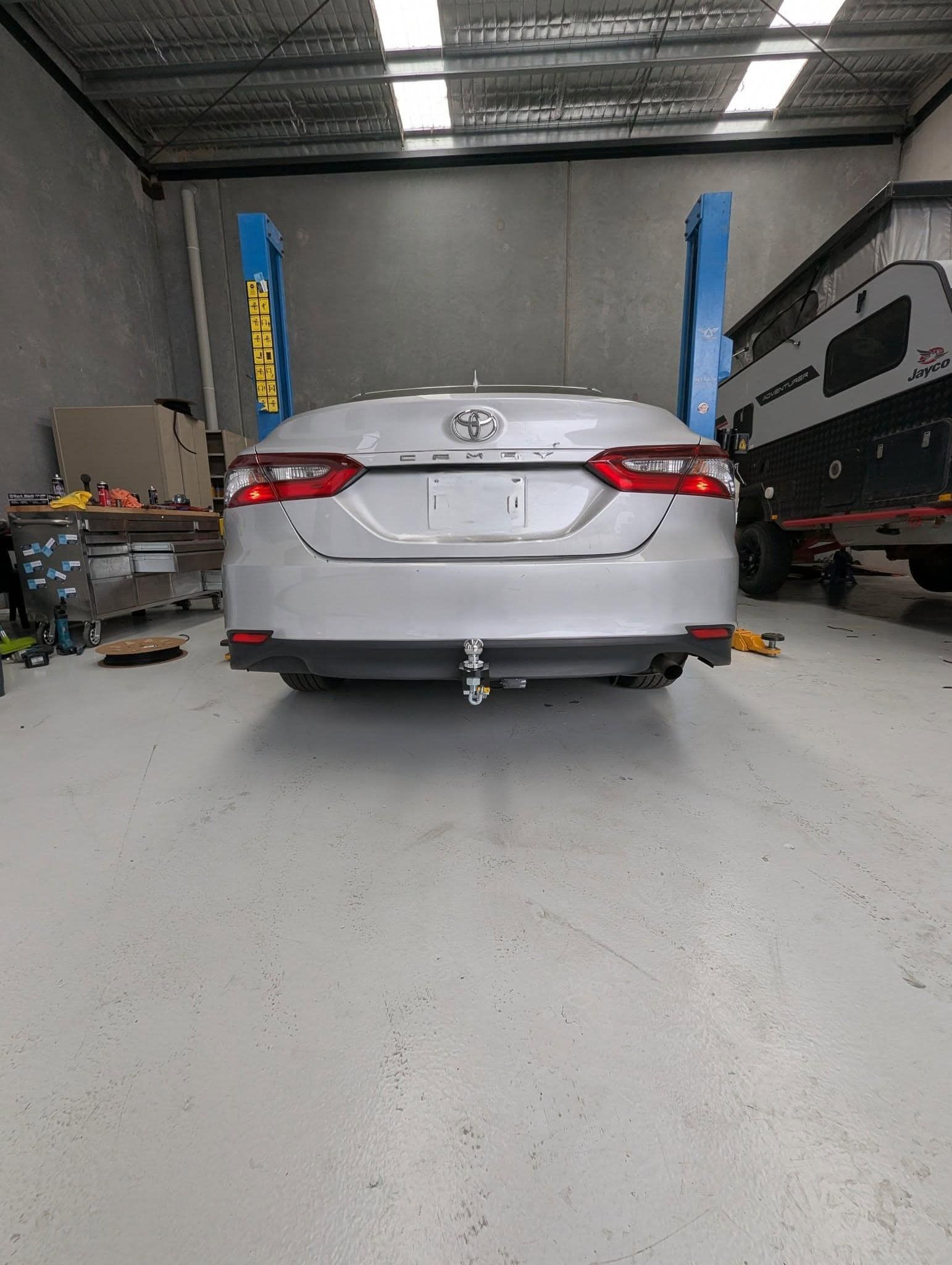 Silver Toyota Camry in a garage, raised on a lift, with a trailer hitch attached. — Caravan and Trailer Clinic Geelong in Breakwater, VIC