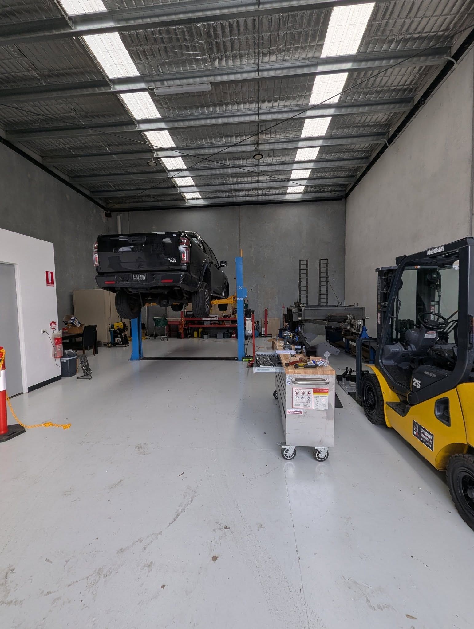 Truck on a lift inside a mechanic's garage with a forklift, tools, and equipment. — Caravan and Trailer Clinic Geelong in Breakwater, VIC