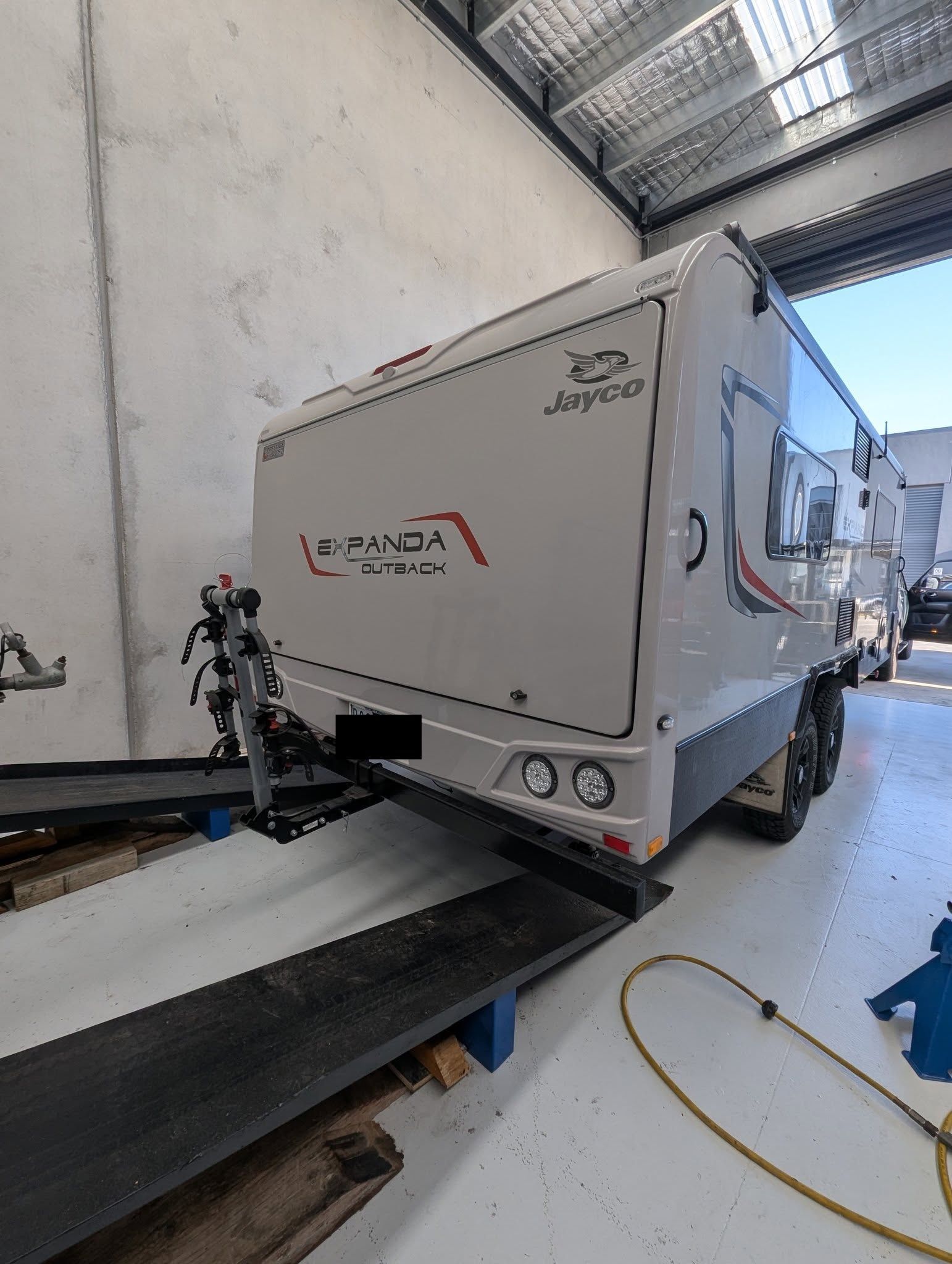 White caravan with red and black accents parked inside a warehouse.  — Caravan and Trailer Clinic Geelong in Breakwater, VIC