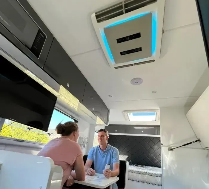 Couple Seated at a Table Inside a Caravan, Beneath an Ac Unit — Caravan and Trailer Clinic Geelong in Breakwater, VIC