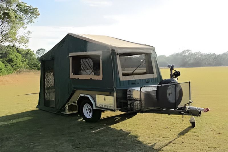 Green and tan pop-up camper trailer on a grassy field with open windows, spare tire, and storage compartments. — Caravan and Trailer Clinic Geelong in Breakwater, VIC