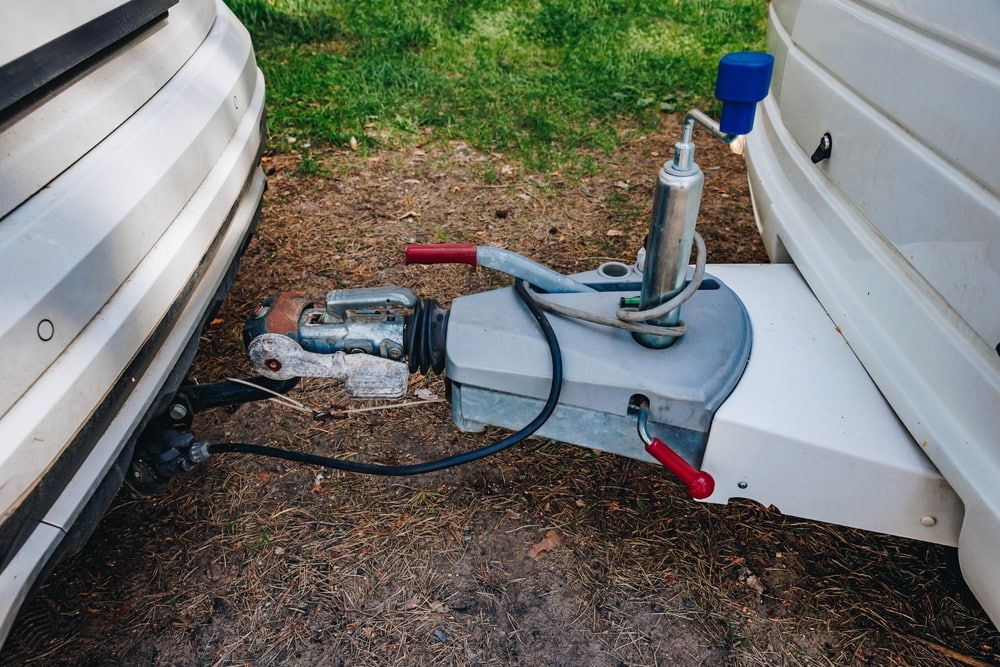 Car and caravan hitch connected, gray and white with a red lever in a grassy area. — Caravan and Trailer Clinic Geelong in Breakwater, VIC