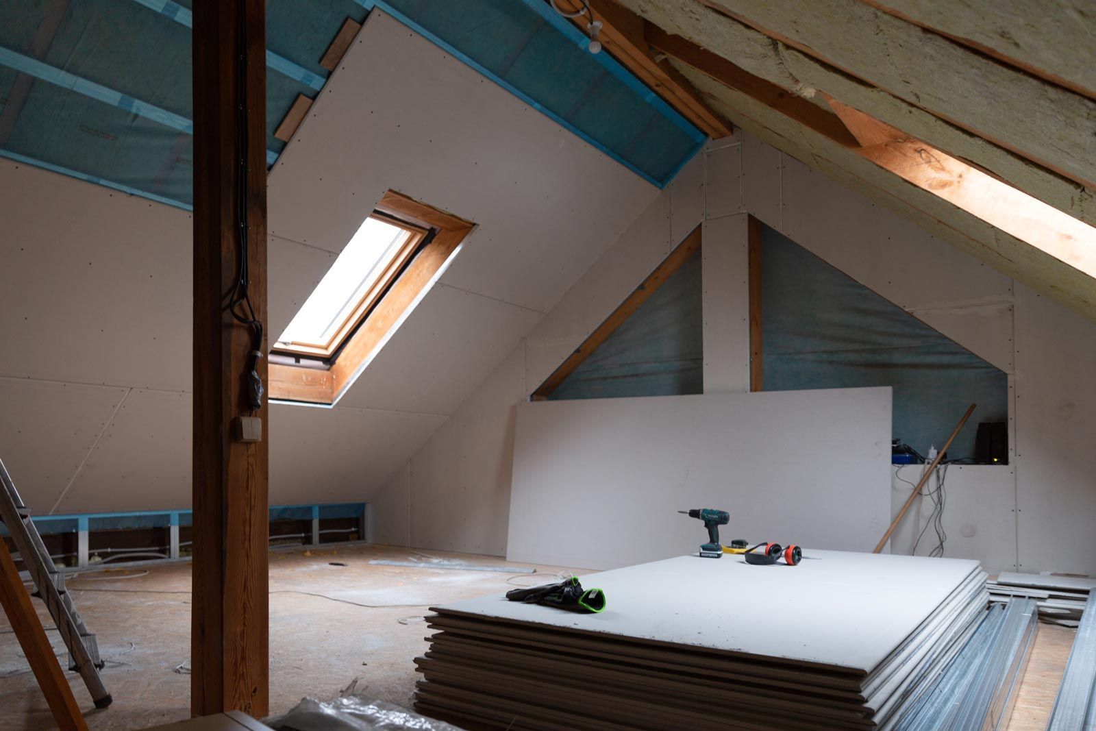 An attic is being remodeled with a skylight and a stack of drywall.