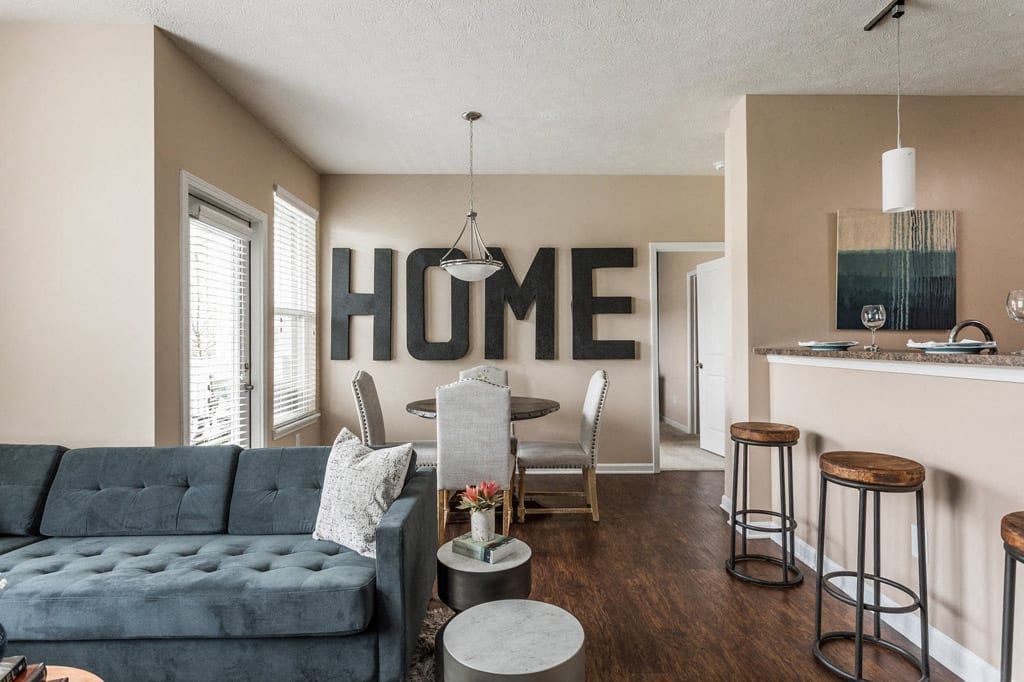 A living room with a couch and a sign on the wall that says home at Maple Knoll Apartments.