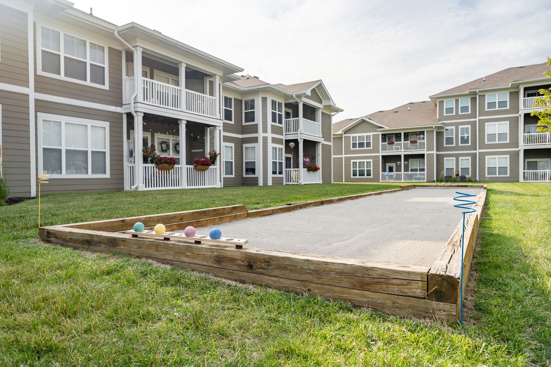 A bocce ball court in front of a large apartment building at Maple Knoll Apartments