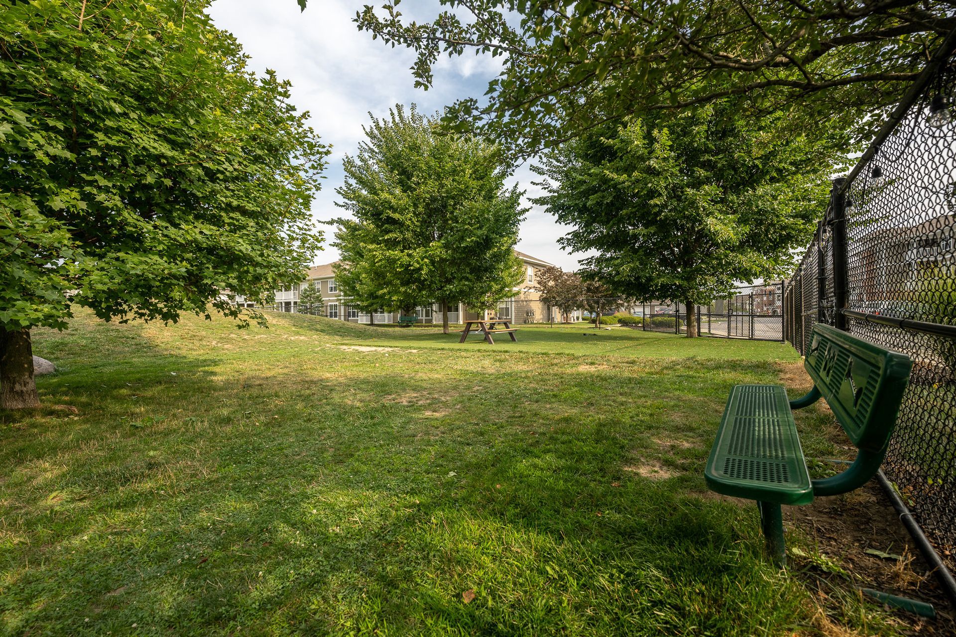 A green bench is sitting in the middle of a park at Maple Knoll Apartments