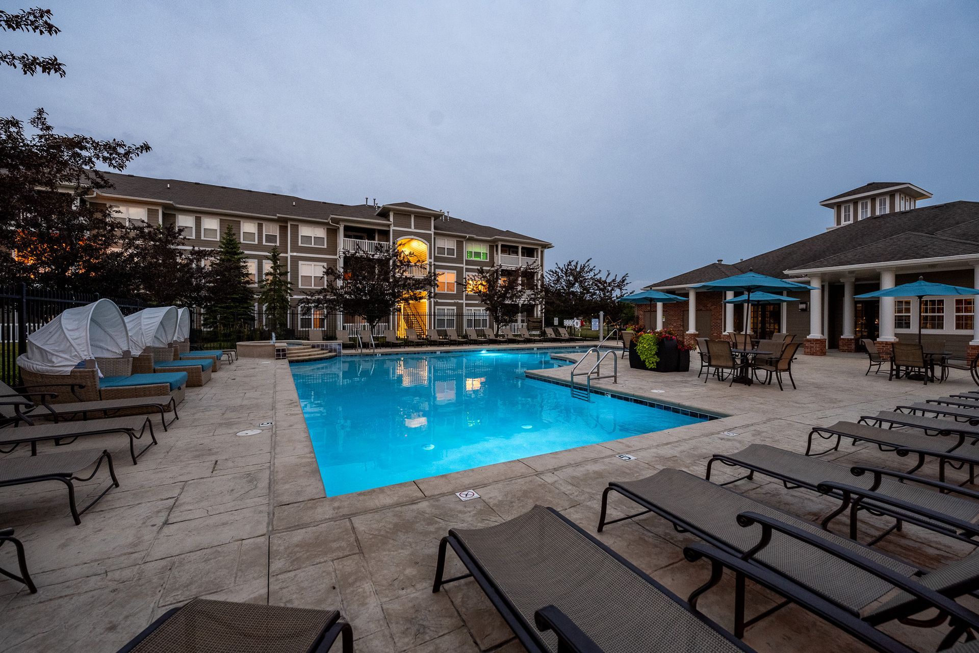 A large swimming pool surrounded by lounge chairs and umbrellas in front of a building at Maple Knoll Apartments