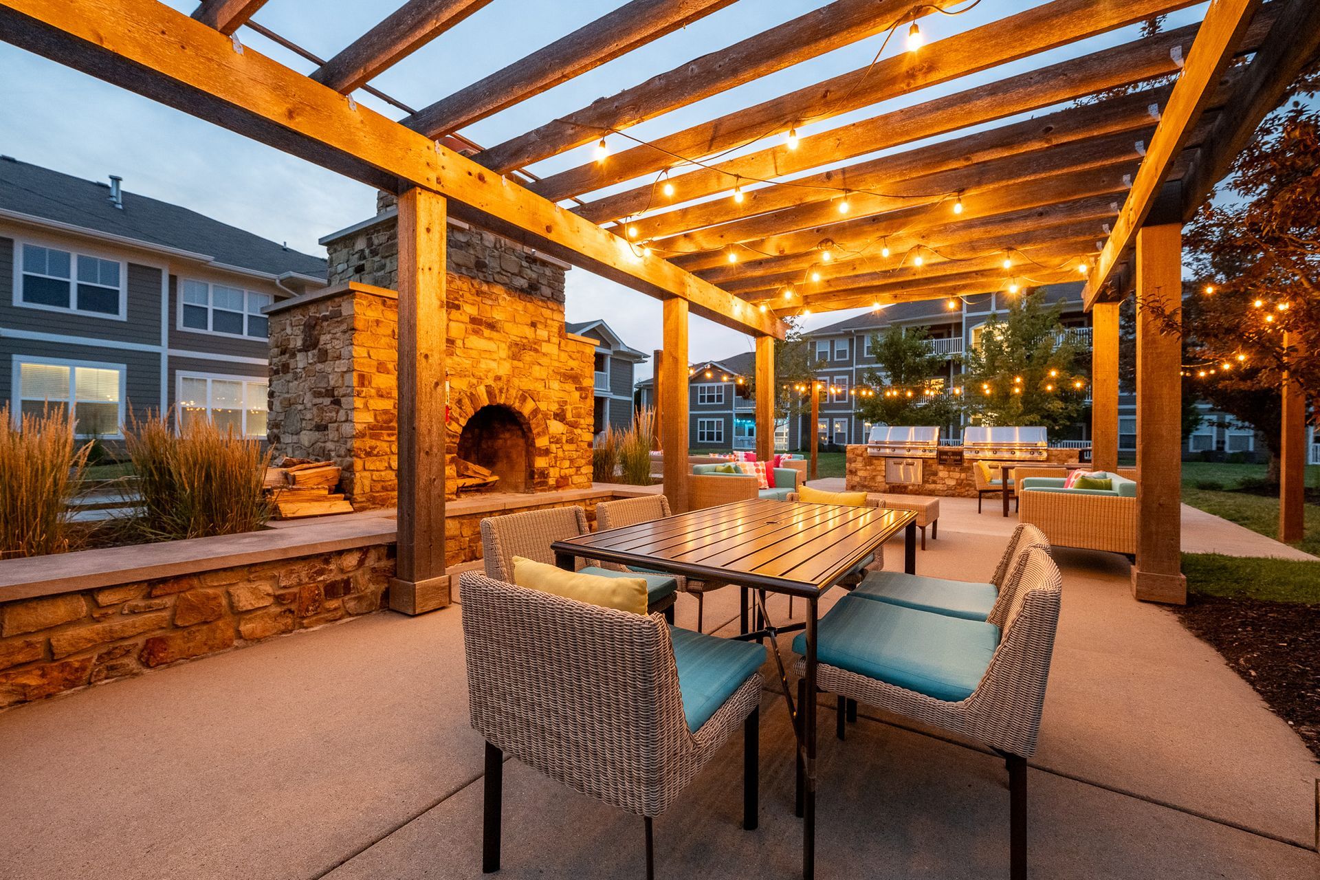 A patio with a table and chairs under a pergola with a fireplace at Maple Knoll Apartments.