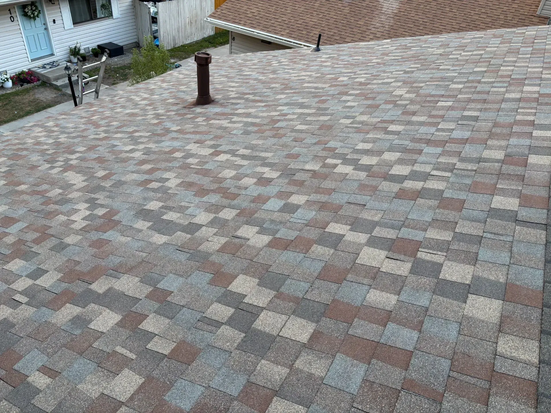 Roof with brown, gray, and tan asphalt shingles. Dark chimney stack present.