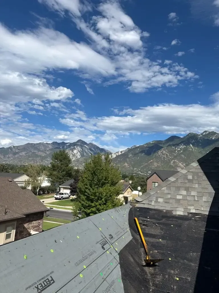View of a partially constructed roof with mountains and blue sky with clouds in the background.