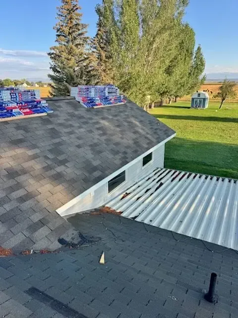 Roof with shingles and stacks of new shingles; open field background.