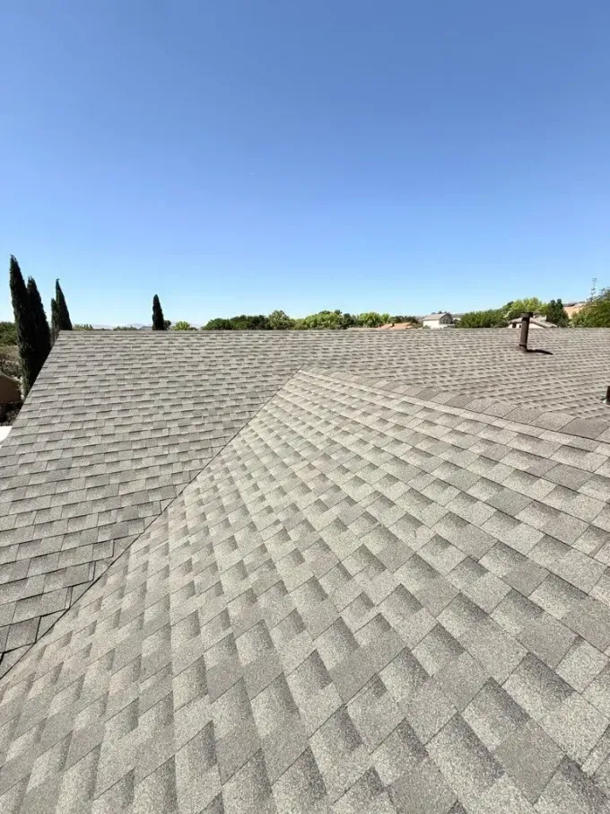 Gray asphalt shingle roof against a clear blue sky, viewed from above.