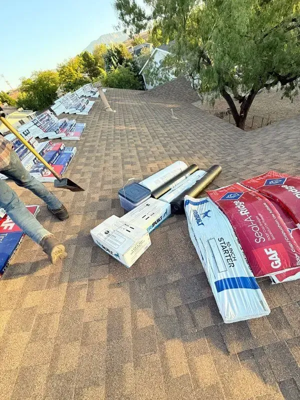 Roofing materials and workers on a rooftop, mountain in background.