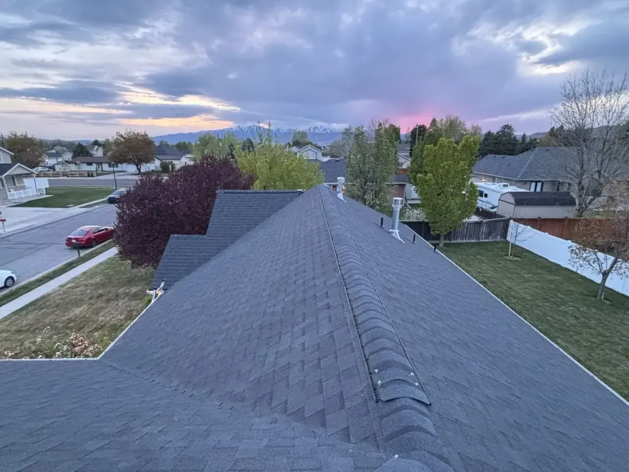 Rooftop view of a residential area under a cloudy sky at dusk; mountains in the distance.