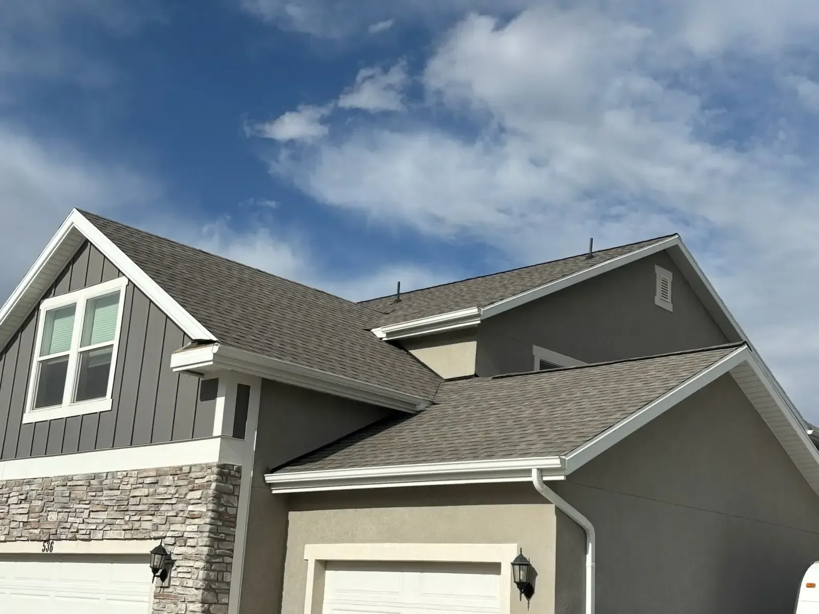 Gray house with a dark gray roof, white trim, and a blue sky with clouds.