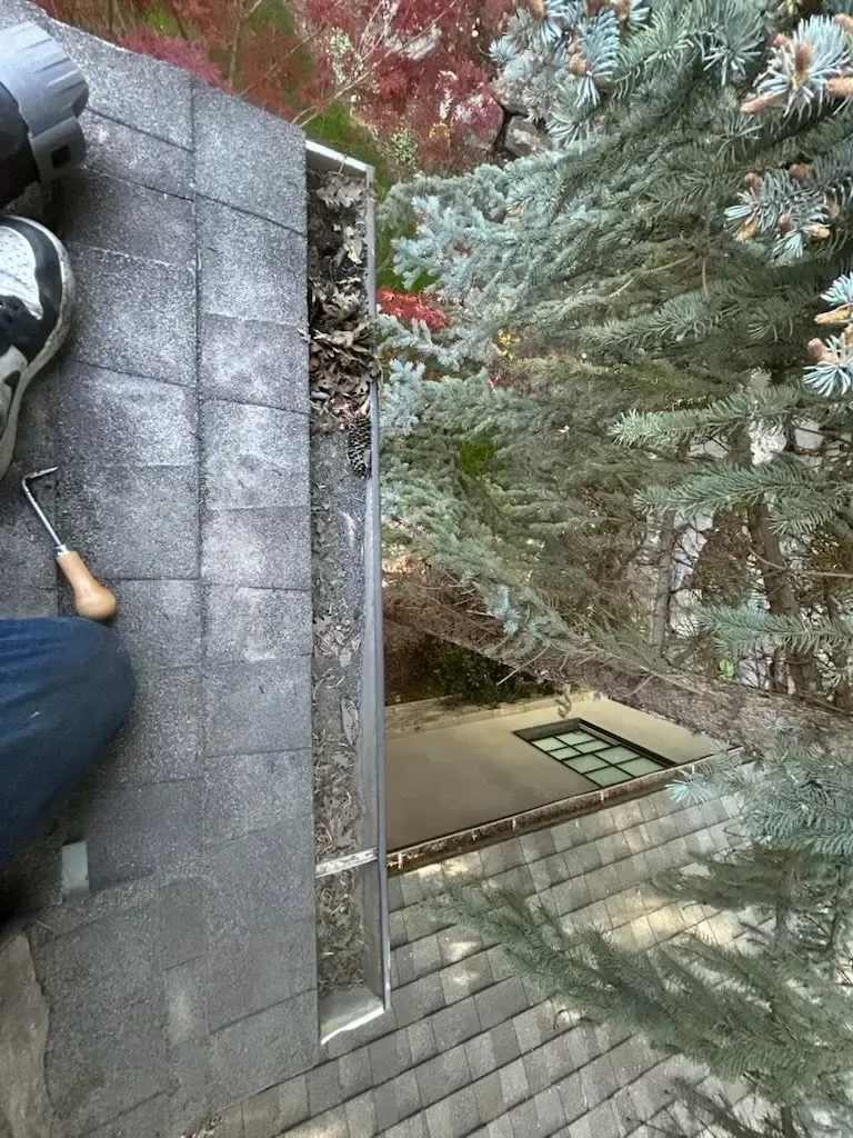 Man cleaning a gutter on a rooftop; debris and a tool are visible.