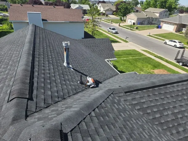 View of a dark shingle roof with a chimney and surrounding suburban neighborhood.