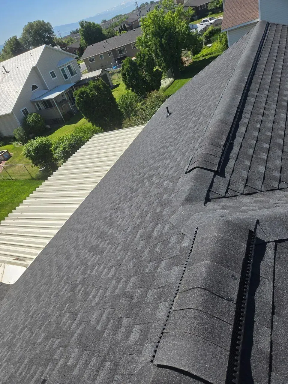 A dark shingle roof slopes down; a white roof and green yard are nearby, in a residential setting.