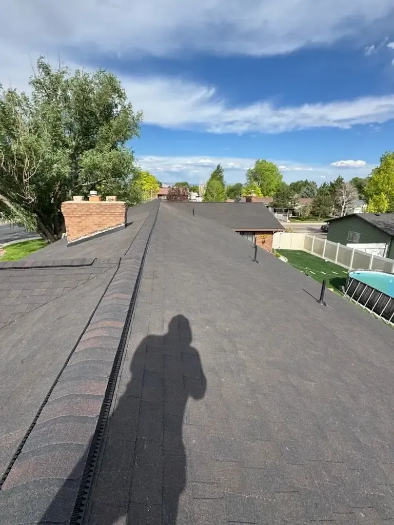 A dark asphalt shingle roof with a brick chimney and shadow of a person on a sunny day.