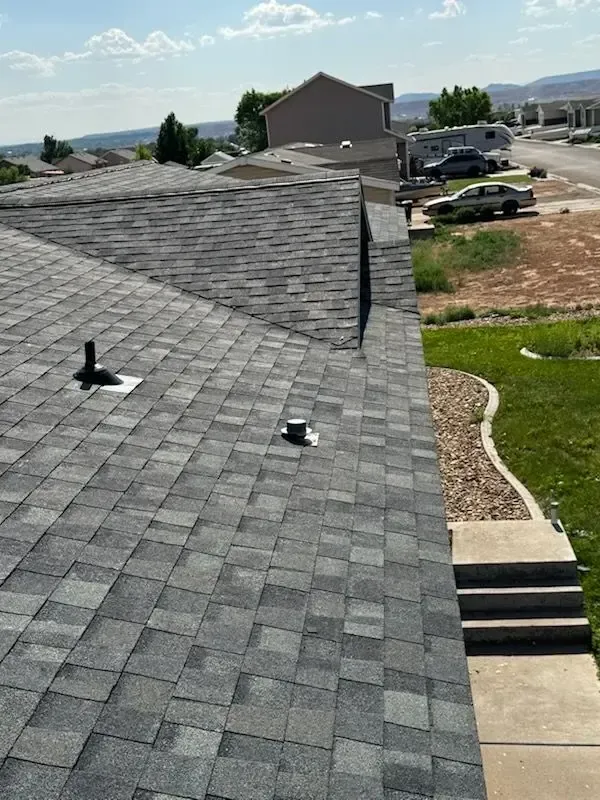 Gray shingle roof of a house with vents, sunny outdoor setting.
