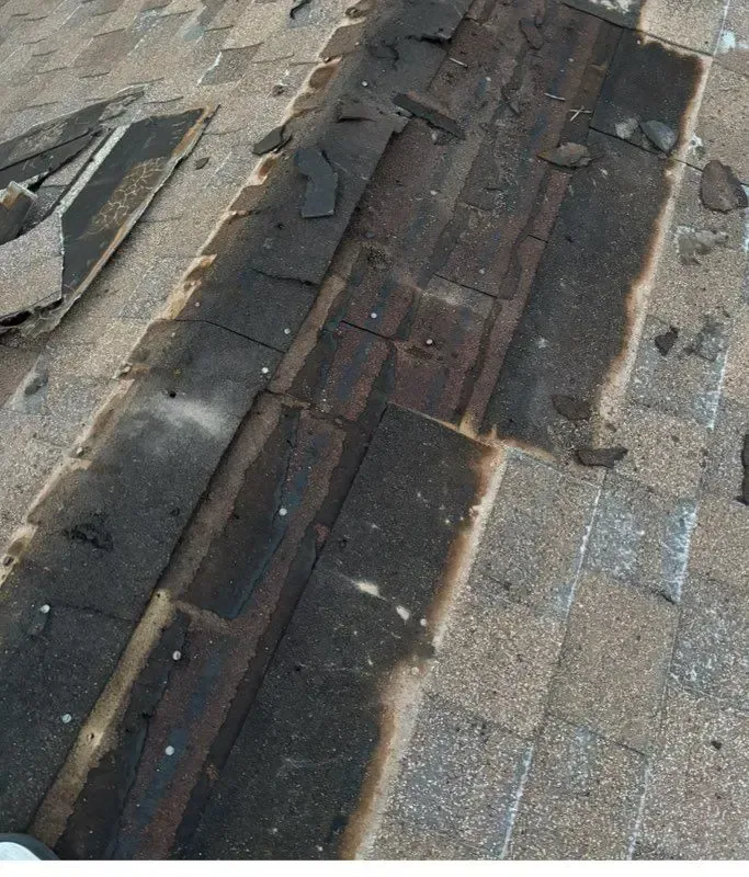 Damaged asphalt shingles on a roof, revealing a dark underlayment.