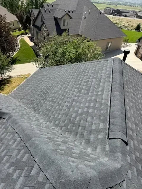 Gray asphalt shingle roof, angled view; houses and greenery in background.