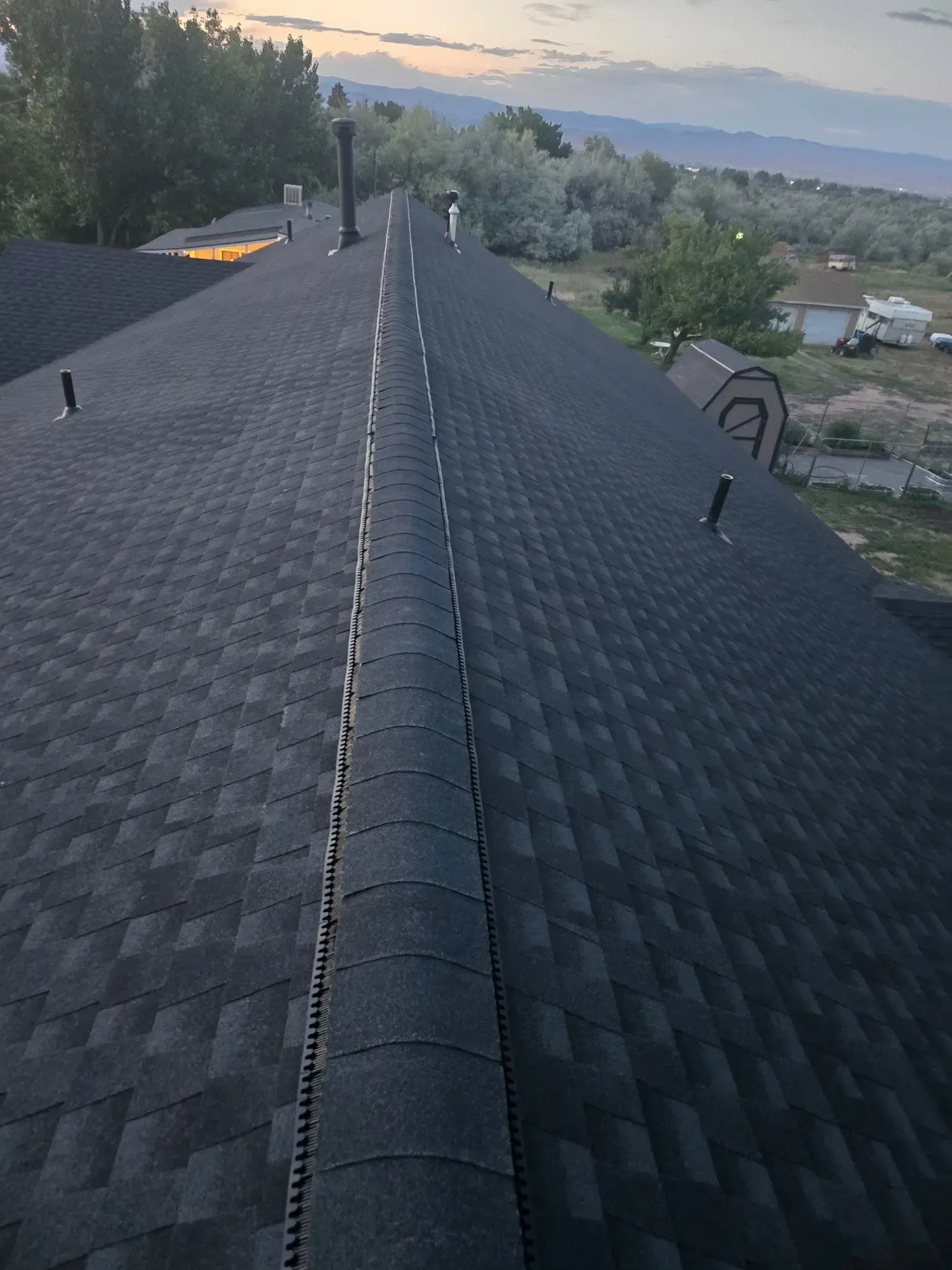 Black asphalt shingle roof with a central ridge, extending towards a hazy mountain backdrop.