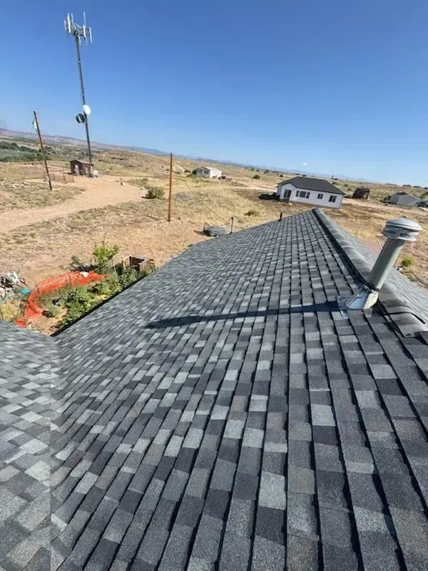 Dark grey shingle roof in sunlight, set against a distant landscape with a cell tower.