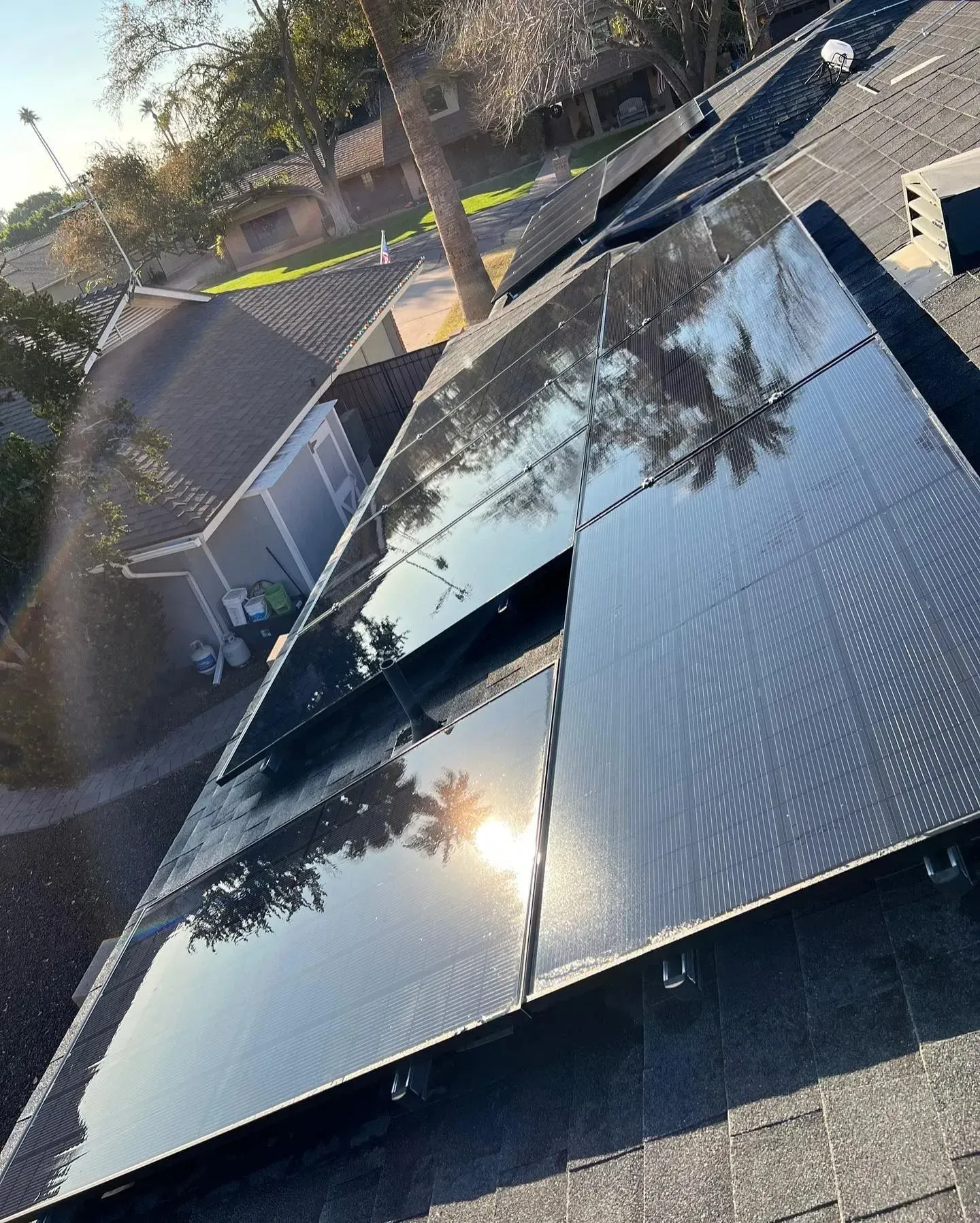 Solar panels installed on a dark rooftop reflecting the sky and sunlight.