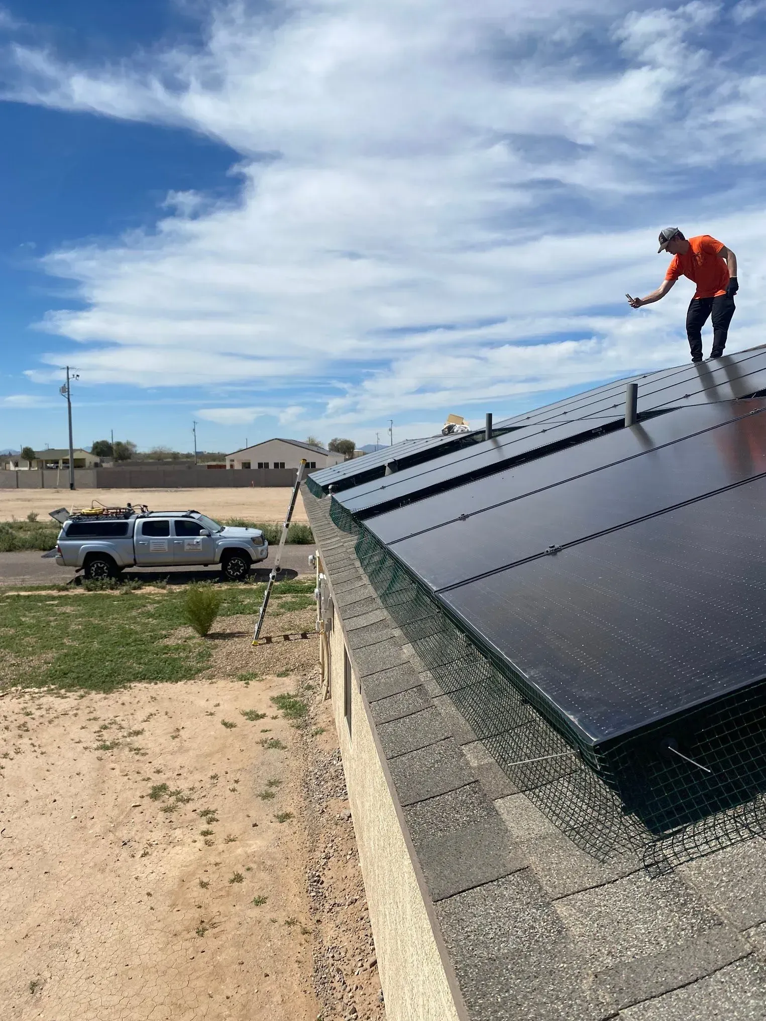 A person in orange shirt on a roof with solar panels, near a truck, sunny day.