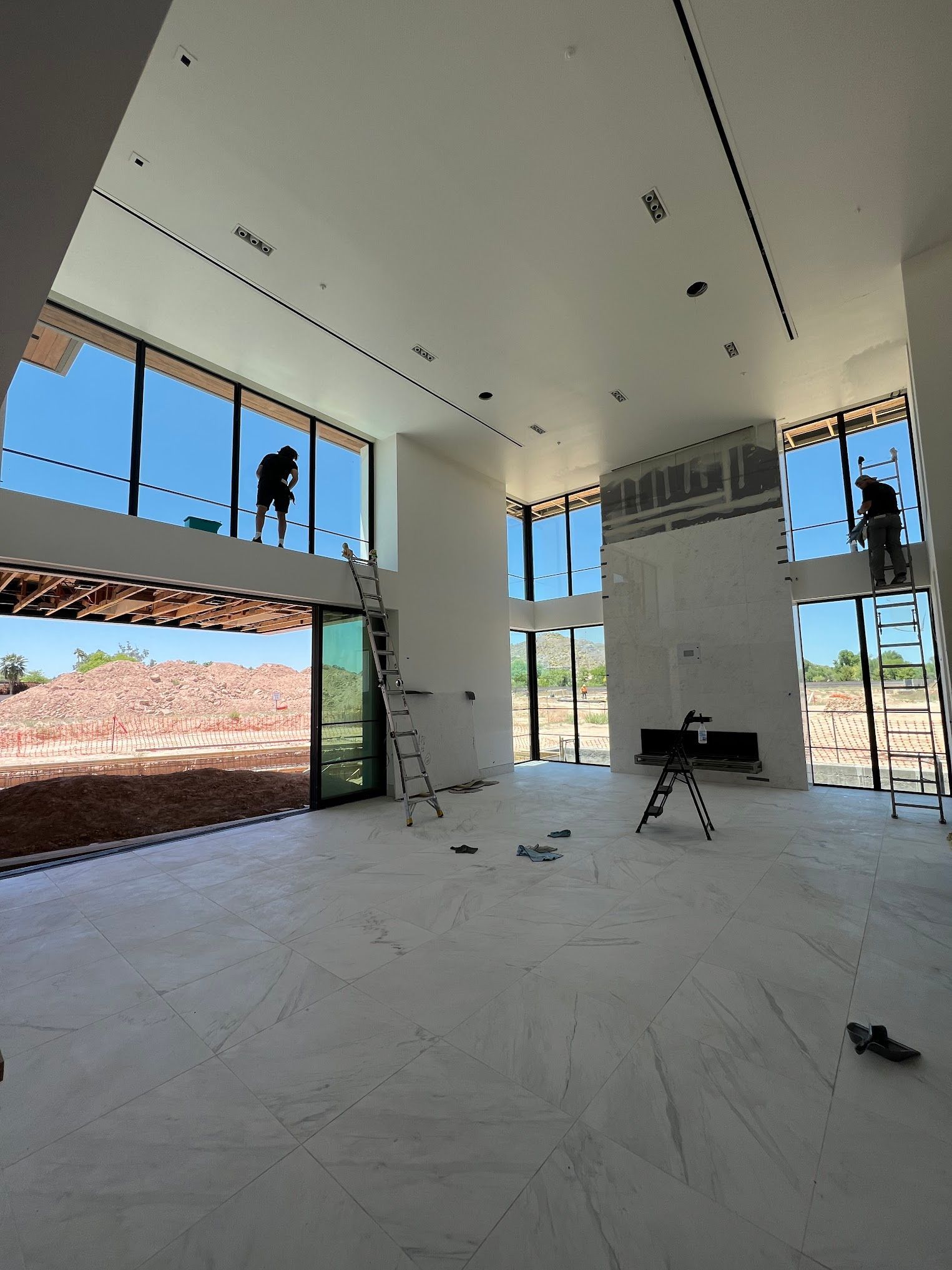 A man is standing on a ladder in a large room with a lot of windows.
