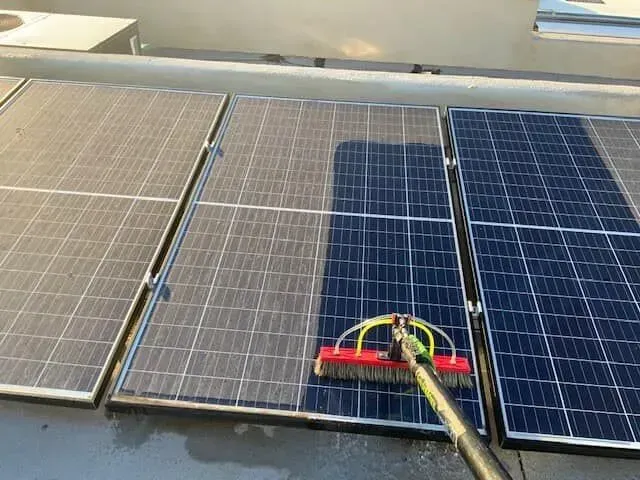 Solar panels being cleaned with a long-handled brush on a rooftop.