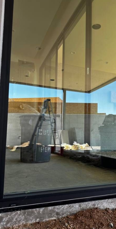 A window with blinds on it and a reflection of a house in the window.