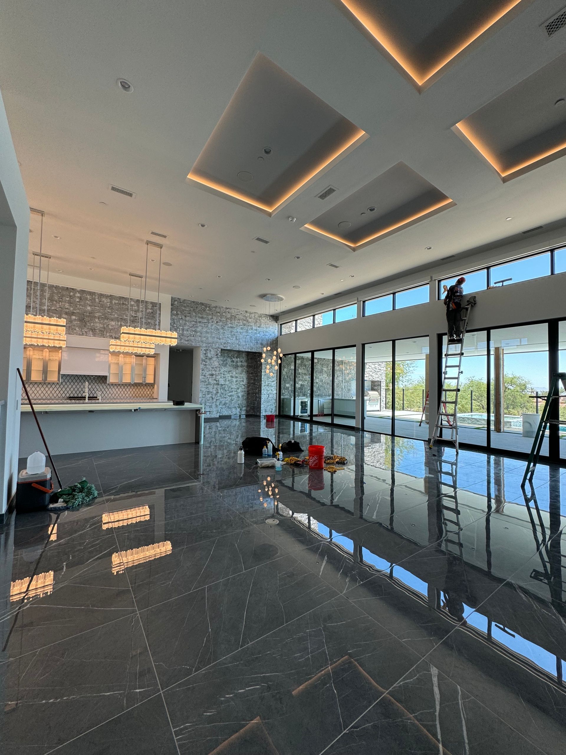 A man is standing on a ladder in a large room with a lot of windows.