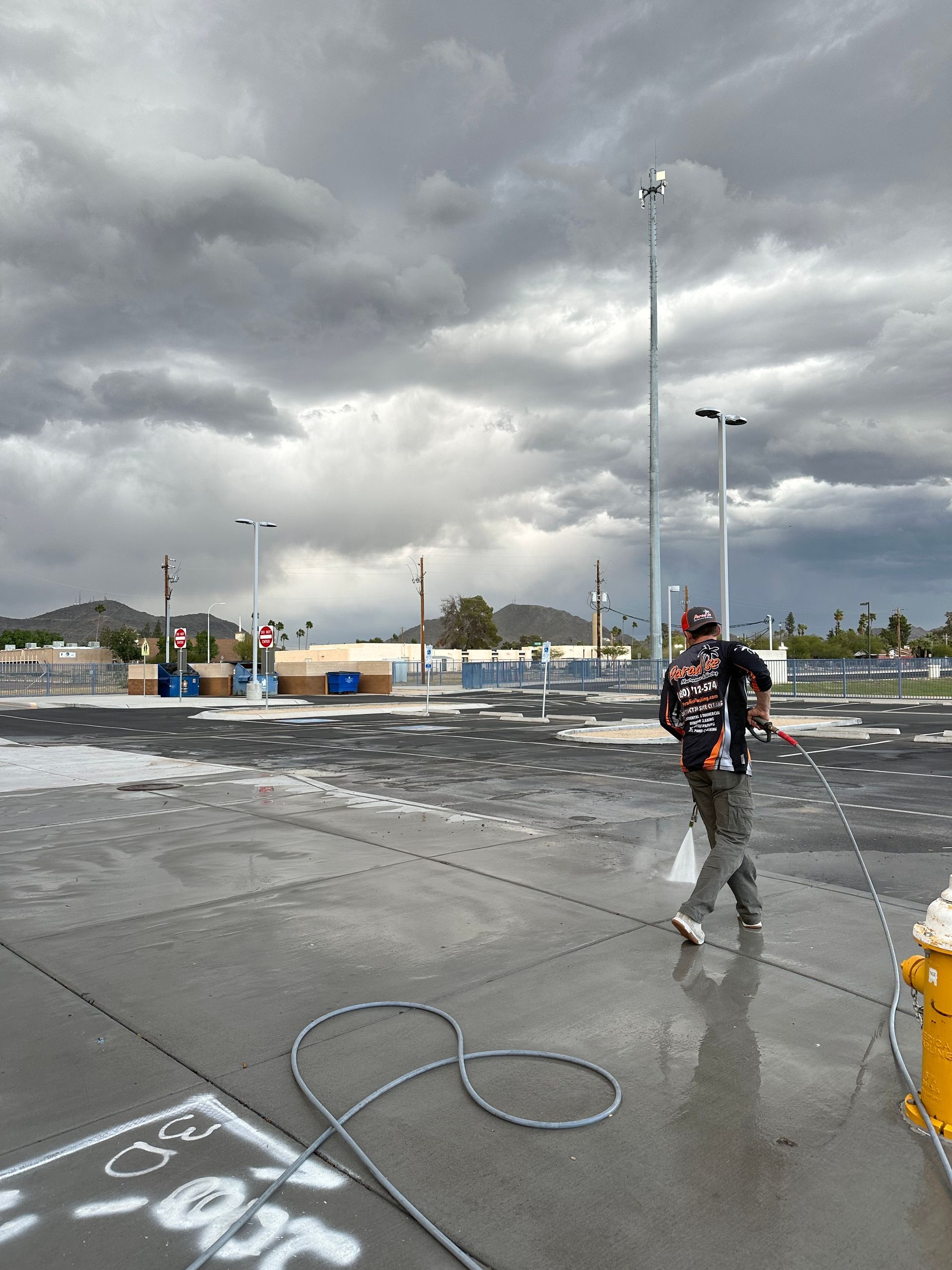 A man is cleaning a parking lot with a hose