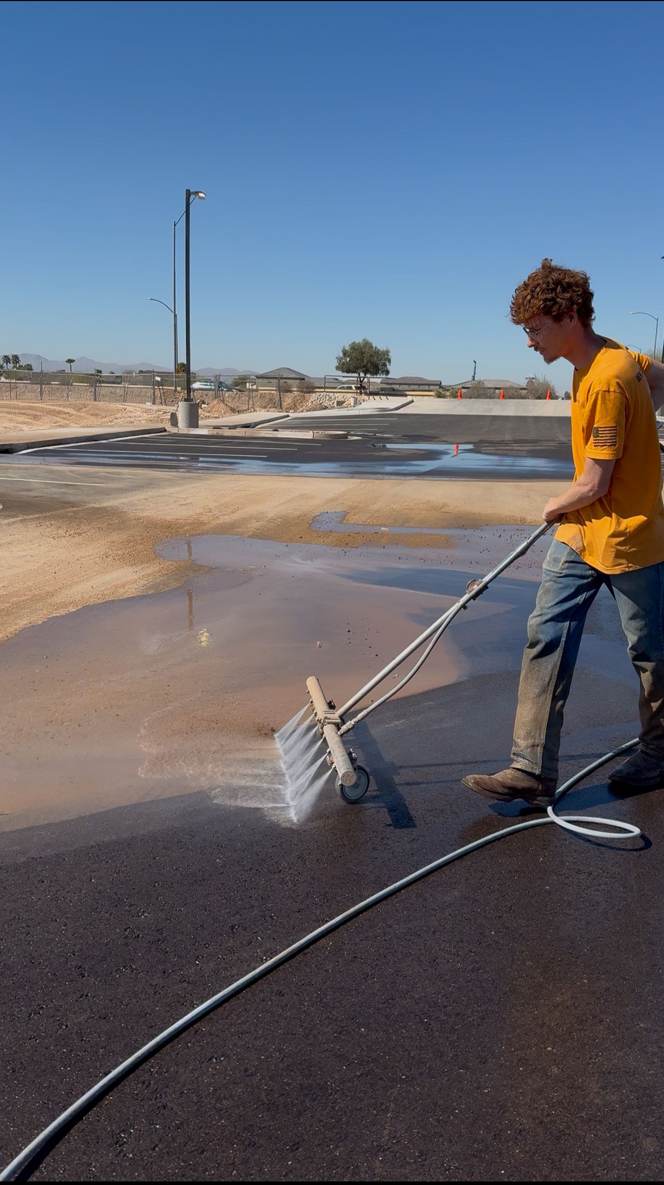 A man in a yellow shirt is using a hose to clean a road.