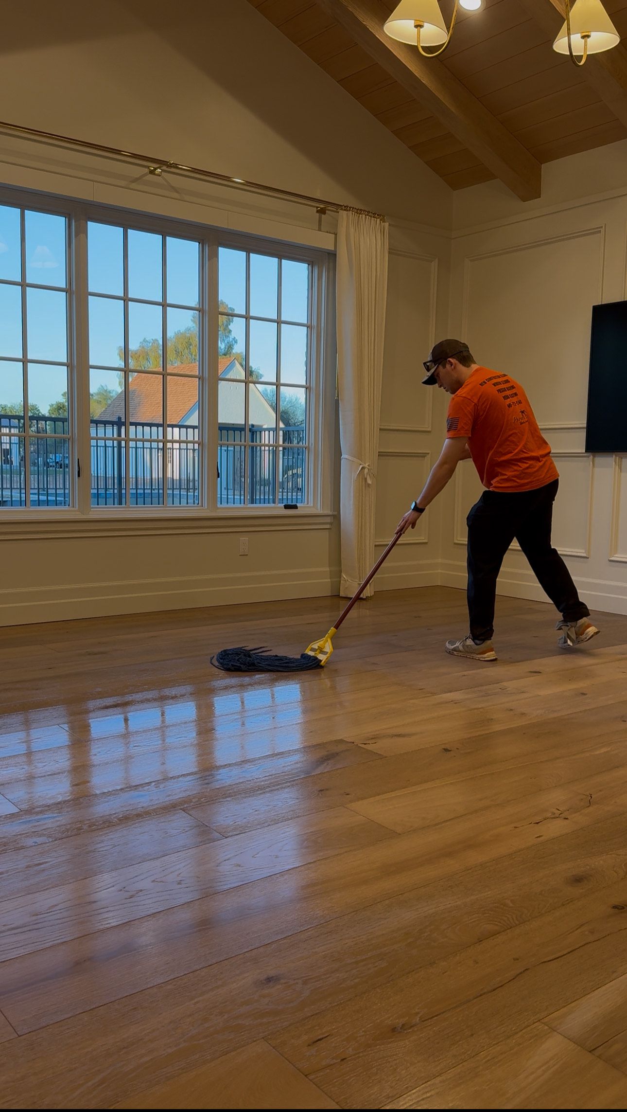 A man is cleaning a wooden floor with a mop.