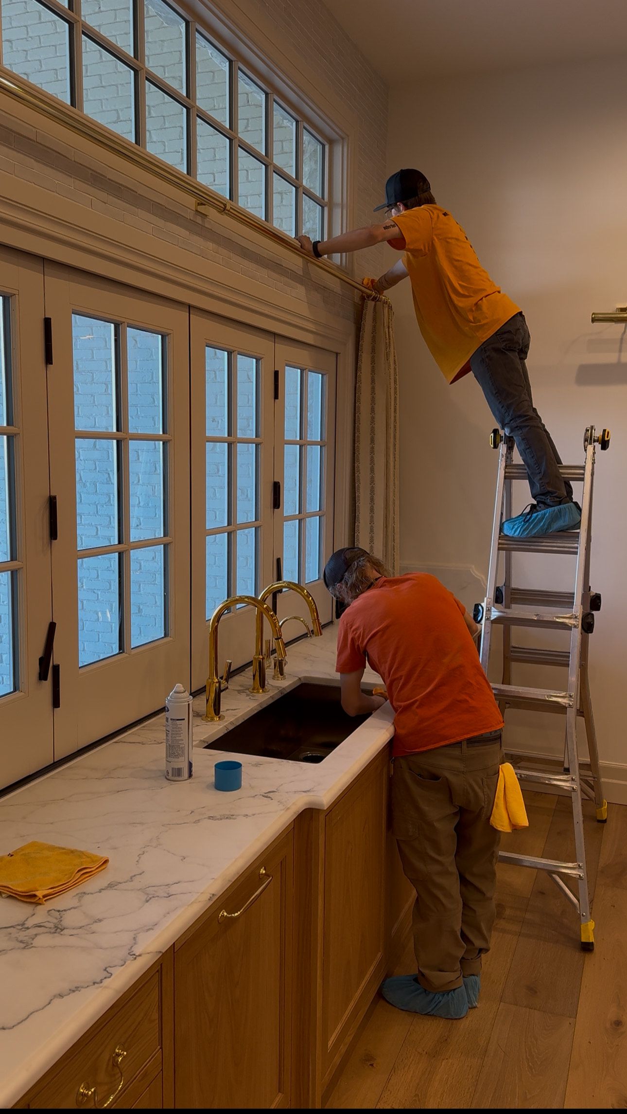Two men are working on a kitchen sink and window