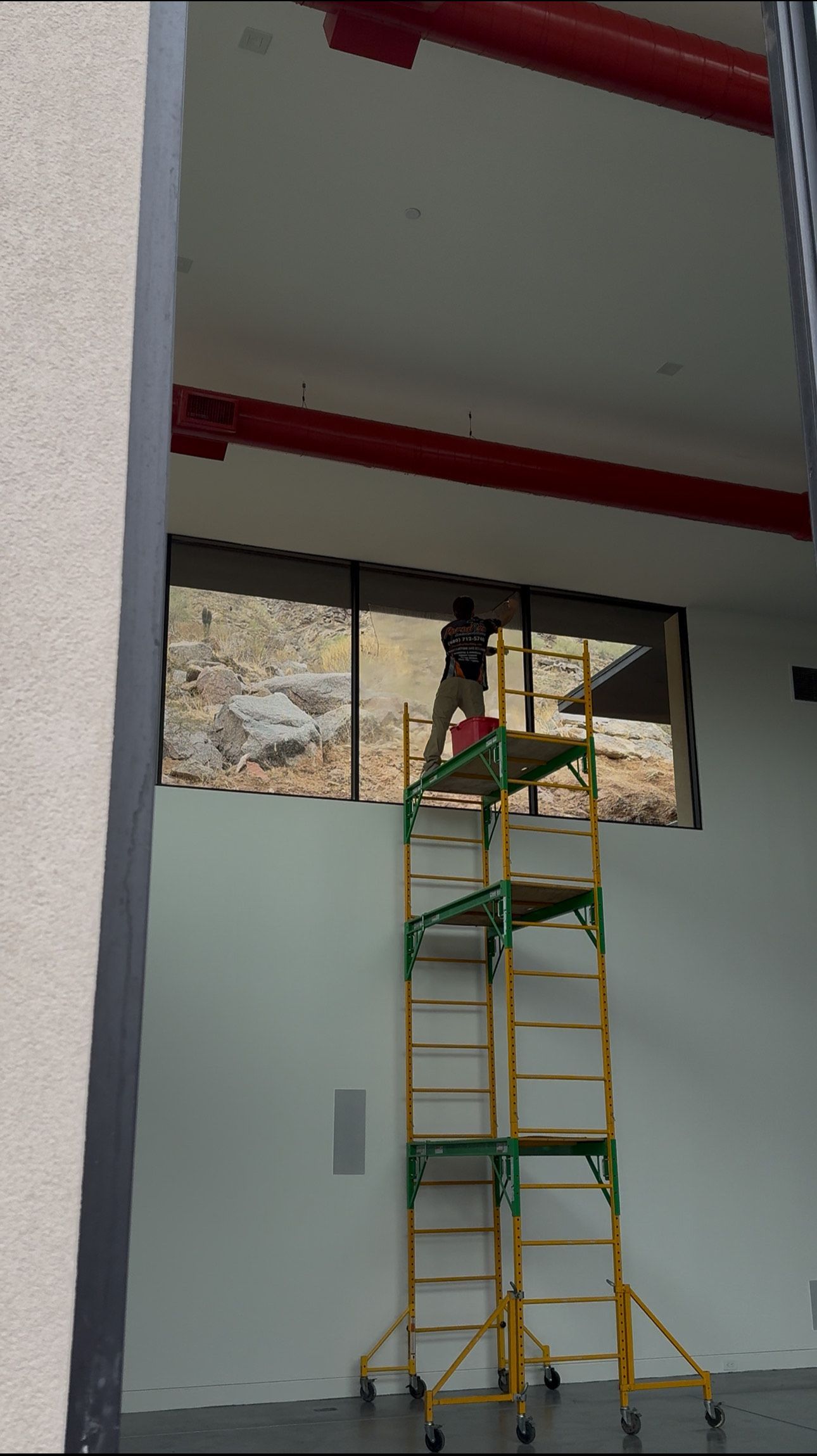 A man is standing on a ladder in front of a window.