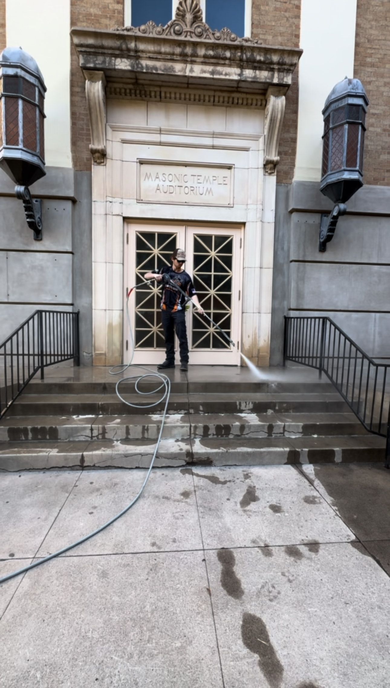 A man is standing in front of a building washing the steps.